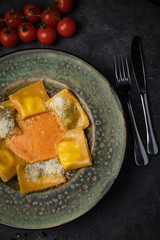 Yellow ravioli with cheese in a plate on a black background