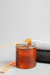Depilation paste in a jar with wooden spatulas, next to towels on a white background. Spa and Shugaring. Self care concept