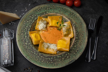 Yellow ravioli with cheese in a plate on a black background
