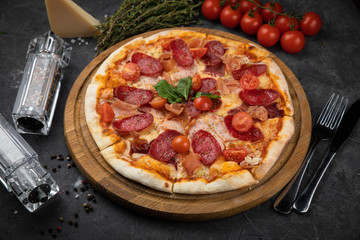 Italian pizza with tomatoes salami, parma, meat and cheese on a black background