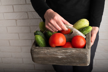 Top view of woman holding a wooden box with raw vegetables. Zucchini, tomatoes and cucumbers in wooden box