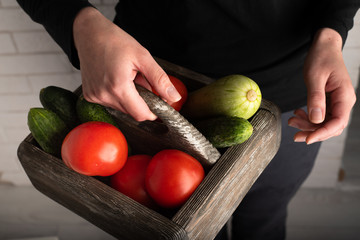 Top view of woman holding a wooden box with raw vegetables. Zucchini, tomatoes and cucumbers in wooden box