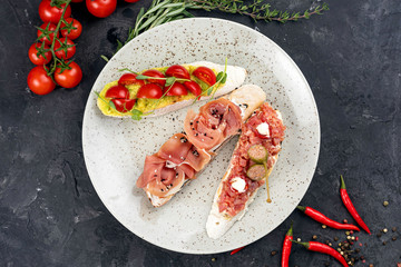 Bruschetta with meat, fish and tomatoes on a dark background

