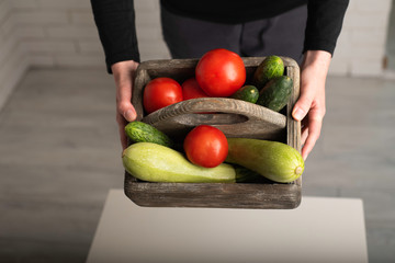 Raw vegetables in a wooden box. Woman holding a box with zucchini, tomatoes and cucumbers. Healthy food