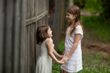 Tender young girls children hold hands and laugh near a wooden fence, intimacy and openness, trust between sisters. The concept of the relationship of siblings and childhood., Sincere emotions.