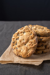 Close-up of a stack of chocolate chip cookies on brown paper and dark tablecloth, black background, vertical