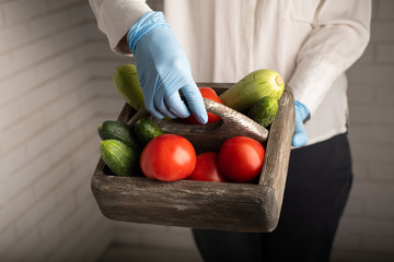Woman in medical gloves holding a wooden box with tomatoes, cucumbers and zucchini
