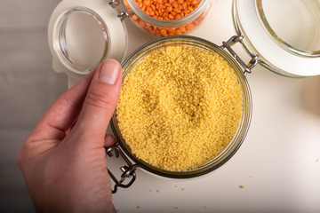 Woman's hand holding a jar with wheat cereals. Jars with lentil and wheat. Top view