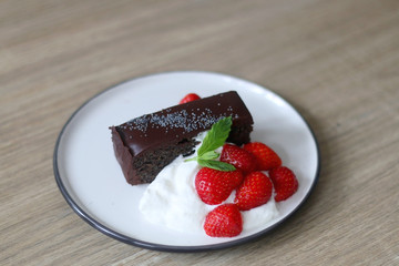 Piece of chocolate and poppy seed cake with whipped cream and strawberries. Selective focus.