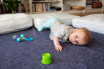 Focused red haired baby trying to crawl to toys, playing on floor at home, improving physical...