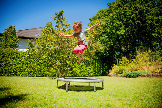 Summer holiday, sport, rest, happy childhood concept. Little cute child girl having fun outdoors and she jumping on a trampoline. Horizontal image.