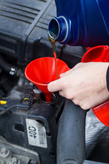 Man uses a red funnel to fill the engine oil in a car with a blue canister. Mechatronic oil level expert e-mobility