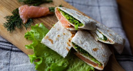 
Healthy food pita bread cutaway appetizer tartilla with soft cheese dill and lettuce on a wooden tray and on a gray kitchen towel