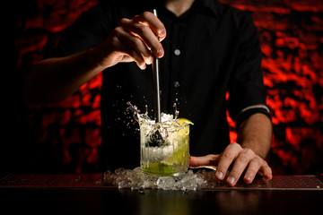 barman making alcoholic cocktail and squeezing juice in glass which splashing out