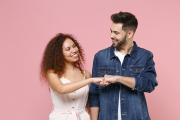 Smiling couple friends european guy african american girl in casual clothes isolated on pastel pink background. People lifestyle concept. Mock up copy space. Giving fist bump, looking at each other.