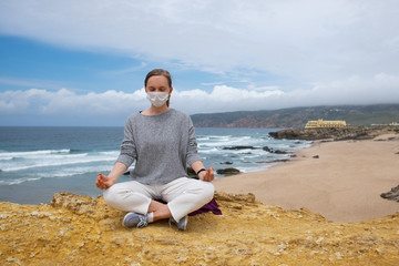 Peaceful woman wearing face mask, meditating in lotus pose, keeping arms in zen gesture. Front...
