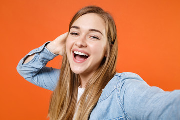 Close up of cheerful young woman girl in casual denim clothes posing isolated on orange background. People lifestyle concept. Mock up copy space. Doing selfie shot on mobile phone, put hand on head.