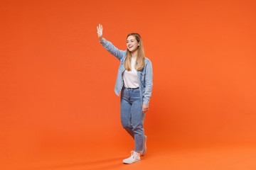 Fototapeta na wymiar Funny young woman girl in casual denim clothes posing isolated on orange background studio portrait. People lifestyle concept. Mock up copy space. Waving and greeting with hand as notices someone.