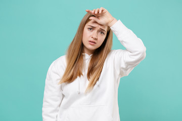 Exhausted tired young woman girl in casual white hoodie posing isolated on blue turquoise background studio portrait. People sincere emotions lifestyle concept. Mock up copy space. Put hand on head.