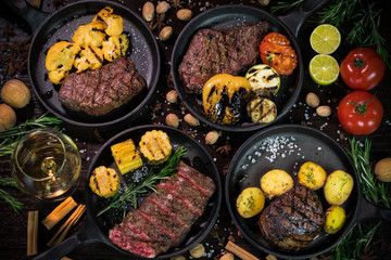 different types of grilled steaks, decorated with tomatoes, walnuts and cinnamon on a dark background
