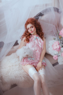 art photo redhead Woman Baroque style frill bow underwear lingerie. Rococo  volume hairstyle hair. Lady holds white rabbit animal posing lies on sofa.  Sexy face pink carnival makeup. Classic royal room Stock