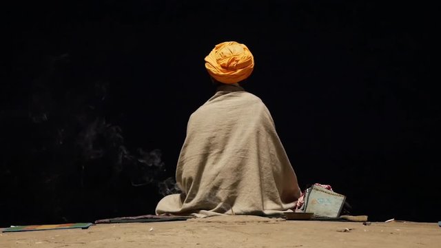 Portrait of sadhu or holy man praying and meditating on Ghats of Varanasi in front of the sacred river Ganges, India, dark time