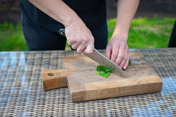 Chef cook slices greens on a wooden board.