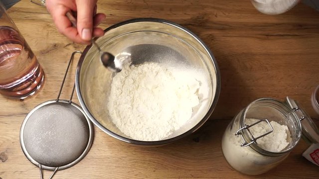 Chef is adding a white salt to a flour for preparing a nice and tasty dough for bakery