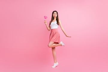 Full body photo of adorable lady send air kisses hold big heart shape lollipop on stick good mood wear white singlet dotted short skirt shoes isolated pastel pink color background