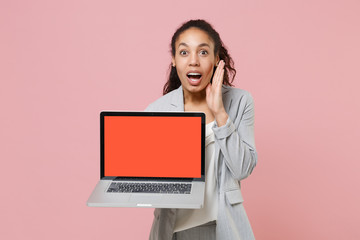Excited african american business woman in grey suit white shirt isolated on pink background. Achievement career wealth business concept. Hold laptop pc computer with blank screen, put hand on cheek.