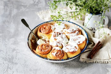 Cinnamon buns in a baking dish with cream cheese curd on a gray background