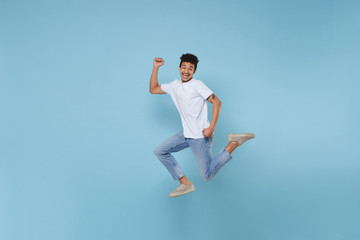Joyful young african american guy in casual white t-shirt posing isolated on pastel blue wall...