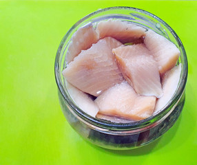slices of slightly salted atlantic herring in a glass jar on a green background