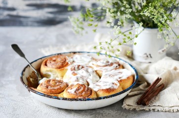 Cinnamon buns in a baking dish with cream cheese curd on a gray background