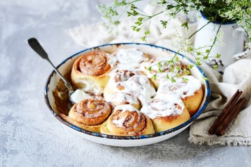 Cinnamon buns in a baking dish with cream cheese curd on a gray background