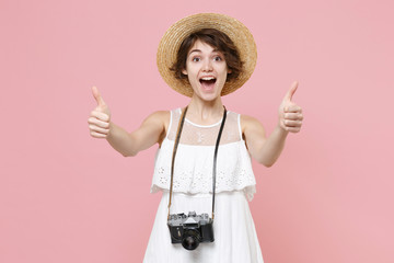 Excited tourist woman in summer dress, hat with photo camera on neck isolated on pink background. Female traveling abroad to travel weekends getaway. Air flight journey concept. Showing thumbs up.