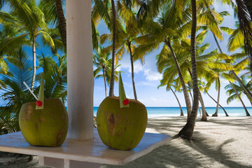 Coconut drinks on table under palm tree leaves umbrella on tropical beach, turquoise water of sea in background. Summer holiday concept