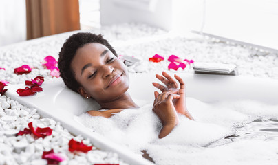 African american woman takes bath with foam and petals