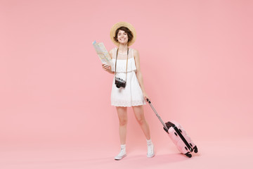 Smiling tourist girl in summer white dress hat with suitcase photo camera isolated on pink background. Female traveling abroad to travel weekends getaway. Air flight journey concept. Hold city map.