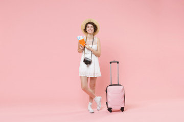 Smiling tourist girl in dress hat with suitcase photo camera isolated on pink background. Traveling abroad to travel weekends getaway. Air flight journey concept. Hold passport tickets boarding pass.