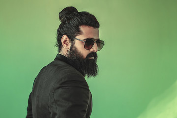 side view of handsome bearded man from the back with a man bun hairstyle posing in studio wearing a...