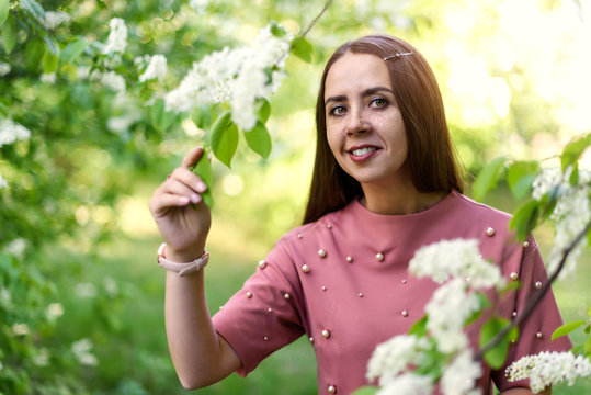 Portrait Of Happy Girl In A Pink T Shirt Holding Flowering Cherry Branch And Looking At The Camera In Sunny Spring Day In Park