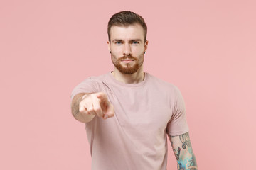 Serious young bearded tattooed man guy in pastel casual t-shirt posing isolated on pink wall background studio portrait. People lifestyle concept. Mock up copy space. Pointing index finger on camera.