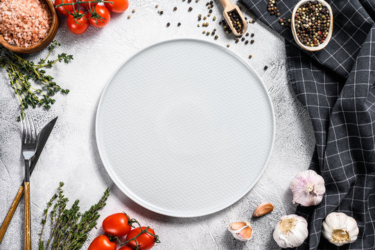 White Empty Plate In Center Of Fresh Raw Greens, Vegetables. Healthy, Clean Eating, Vegan, Dieting Food Concept. White Background. Top View. Copy Space