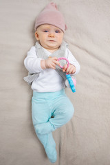 Full length shot of cute baby lying on grey blanket, holding rattle toy, looking at camera....
