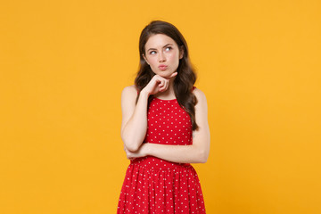 Pensive young brunette woman girl in red summer dress posing isolated on yellow background studio...