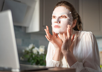 Businesswoman works at home behind a laptop and does facial skin care procedures. Girl adjusts a...