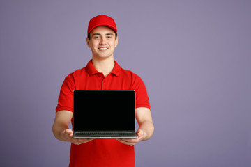 Smiling courier holding laptop with blank screen, isolated on gray background, studio shot