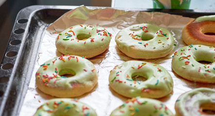Freshly baked donuts with green icing and colorful pastry topping