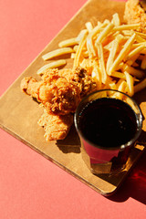 crispy deep fried chicken and french fries served on wooden cutting board with soda in sunlight